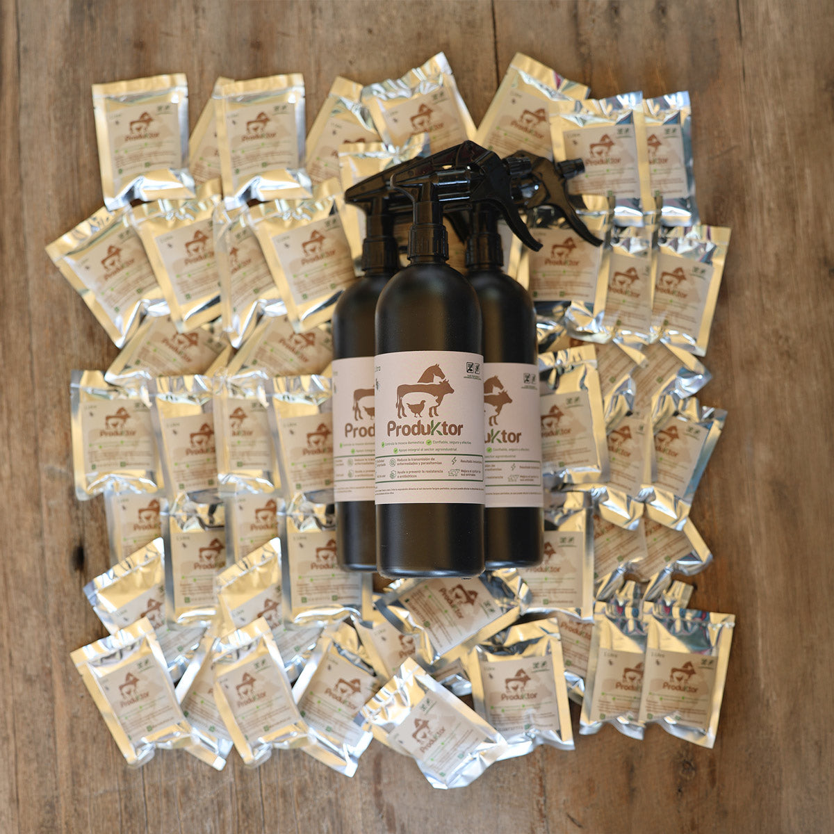 Kit ProduKtor de 40 litros: tres atomizadores ámbar rodeados por los sobres de cebo para moscas, sobre madera.