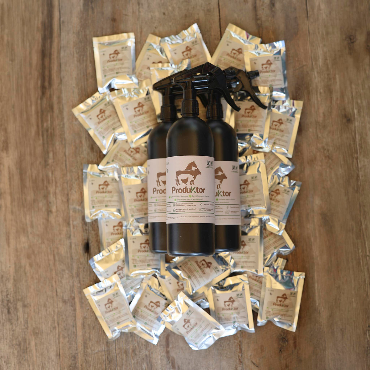 Kit ProduKtor de 30 litros: tres atomizadores ámbar rodeados por los sobres de cebo para moscas, sobre madera.